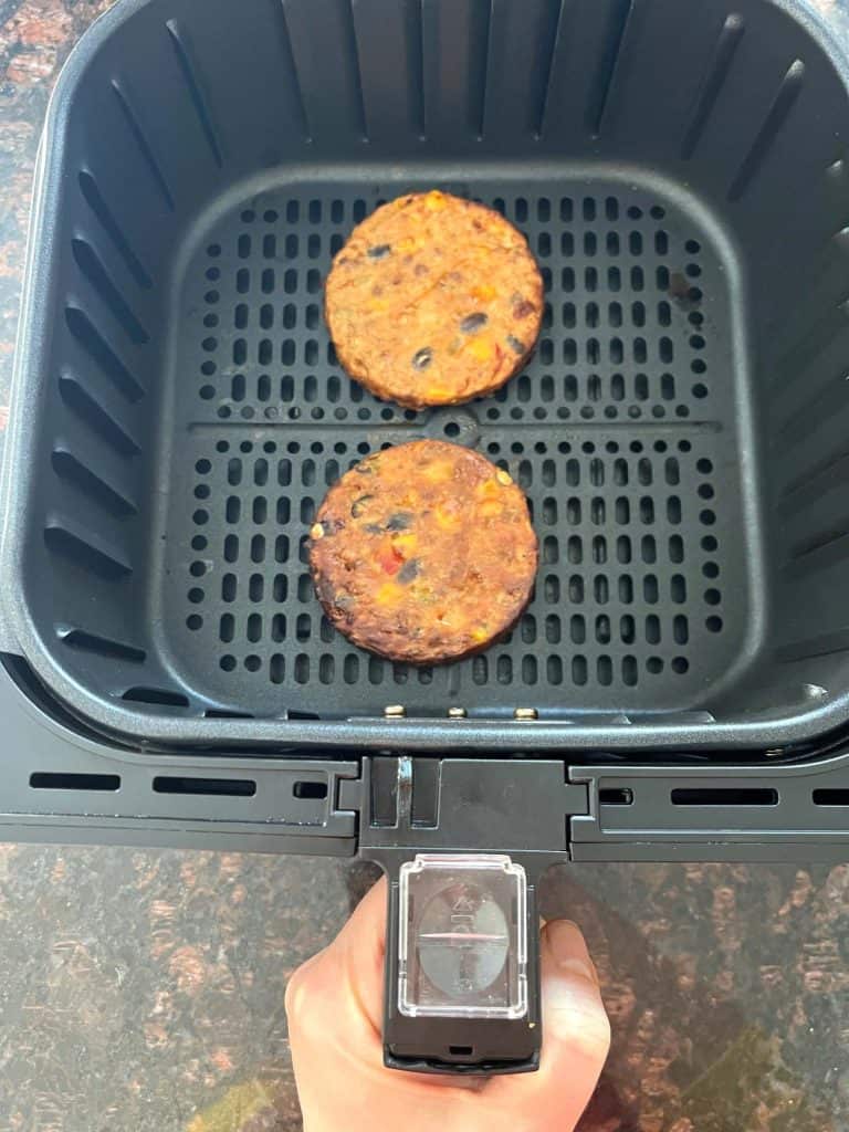 Two cooked black bean burgers in an air fryer basket, showing the crispy result after air frying from frozen.