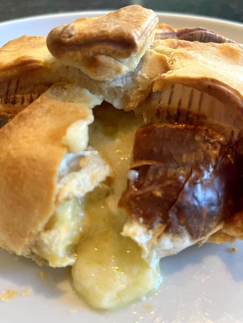 Melted brie cheese oozing out of a freshly sliced golden brie en croute on a plate.