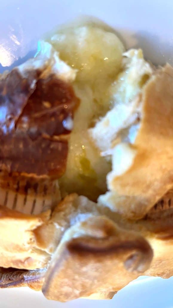Close-up of gooey melted brie cheese flowing out of sliced brie en croute pastry on a white plate.