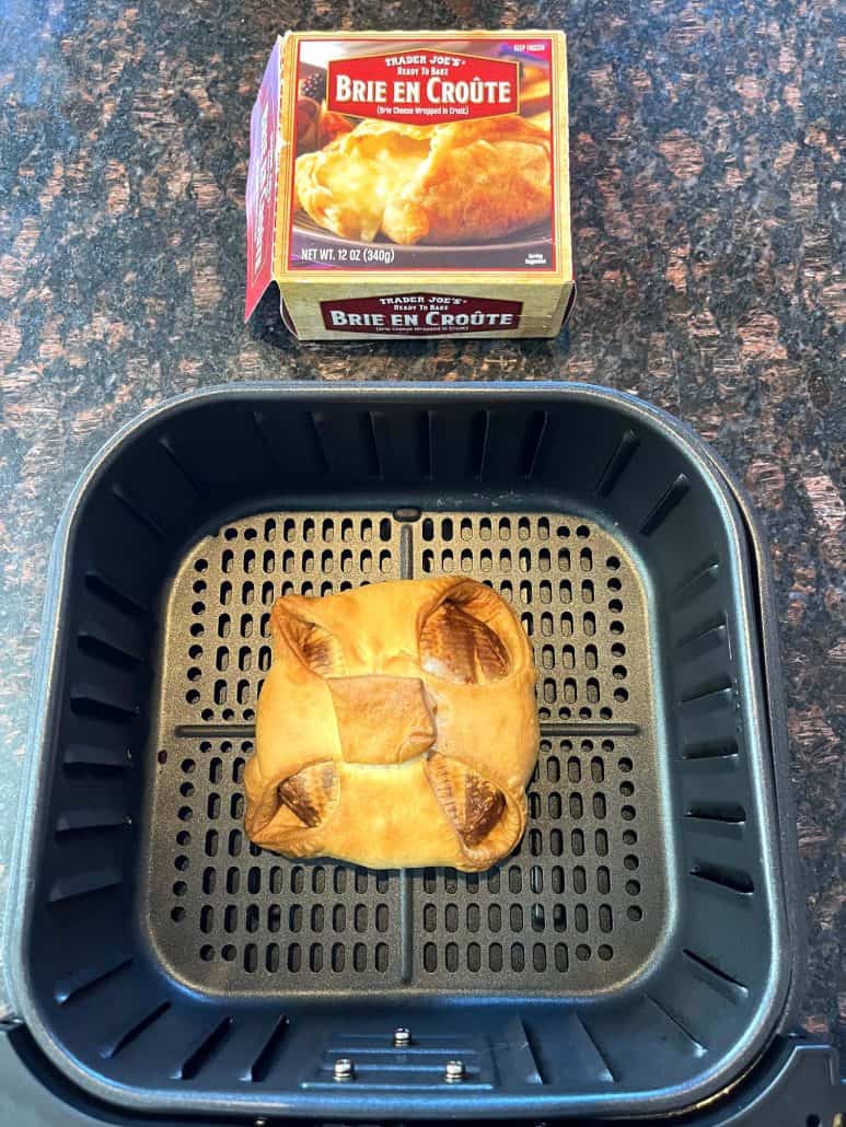 Cooked Trader Joe’s frozen brie en croute in air fryer basket with product box in the background.