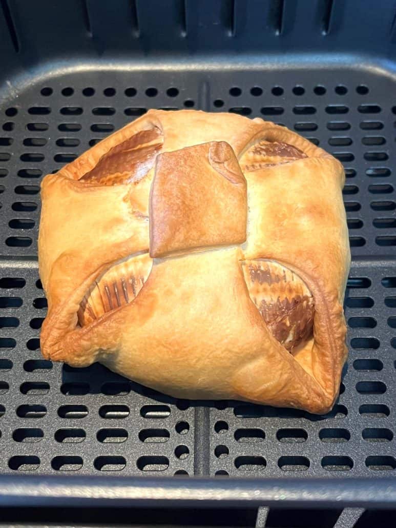 Close-up of golden brown brie en croute in the air fryer basket, just finished cooking.