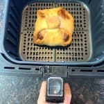 Golden brown frozen brie en croute freshly cooked in the air fryer basket, ready to rest before serving.