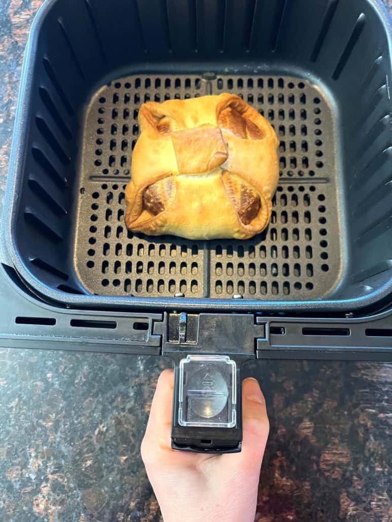 Golden brown frozen brie en croute freshly cooked in the air fryer basket, ready to rest before serving.