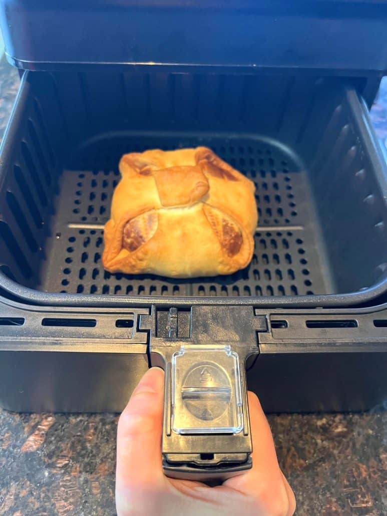 Air fryer basket with fully cooked and golden frozen brie en croute.