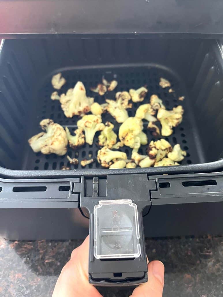 Air fryer basket filled with cooked frozen cauliflower, showing how crispy and browned the cauliflower.