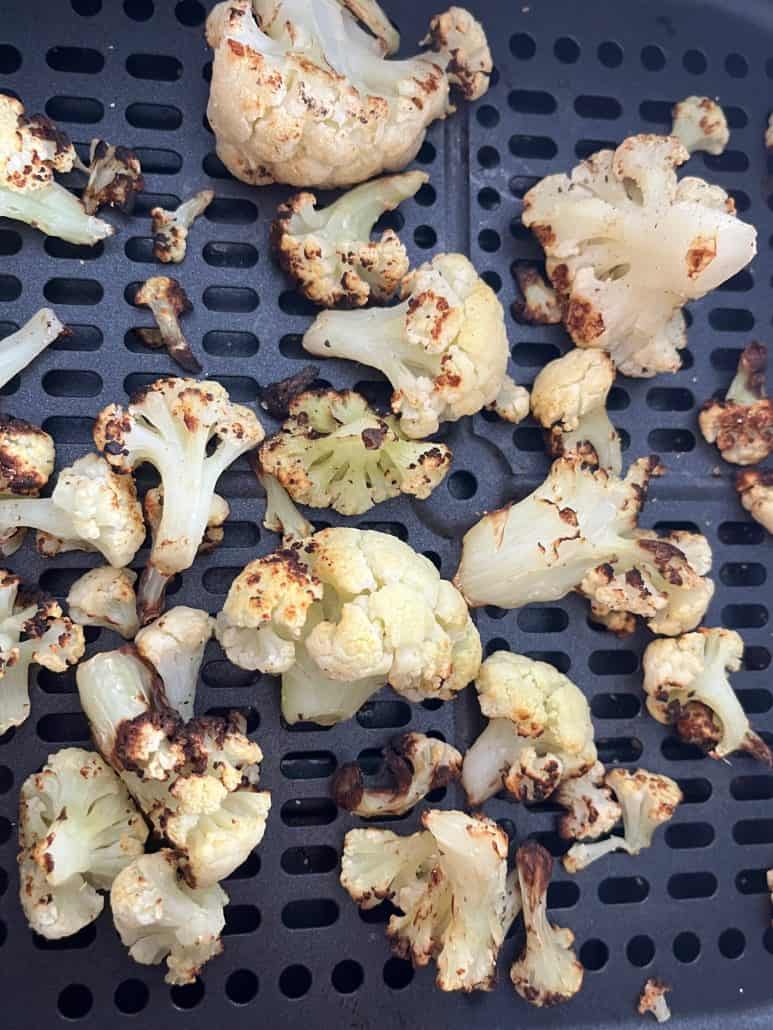 Close-up of roasted frozen cauliflower in the air fryer basket, showing the crispy, browned edges from this simple air fryer method.