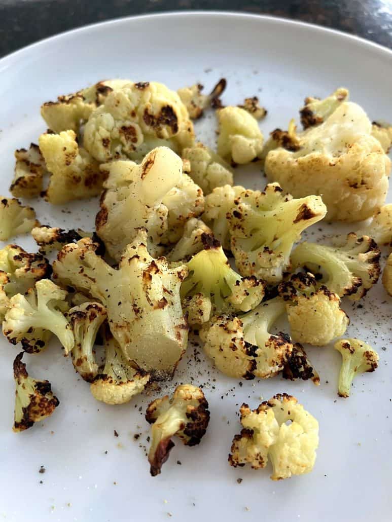 Close-up of air-fried cauliflower on a white plate, showing crispy edges and seasoning.