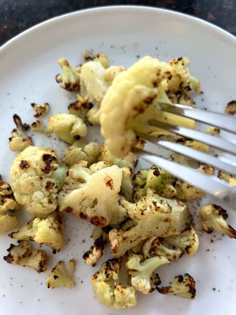 Fork holding a piece of crispy air-fried cauliflower over a plate, showing the delicious texture and browning from cooking frozen cauliflower in the air fryer.