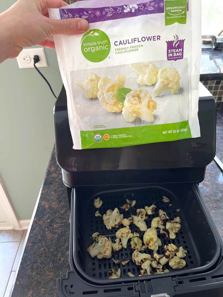 Bag of frozen cauliflower held over an air fryer basket.
