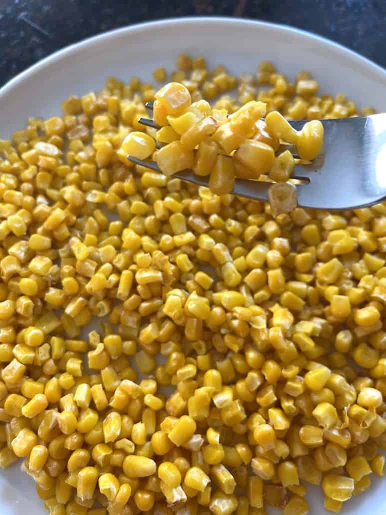 Crispy air fryer corn on a white plate with a forkful of corn lifted.