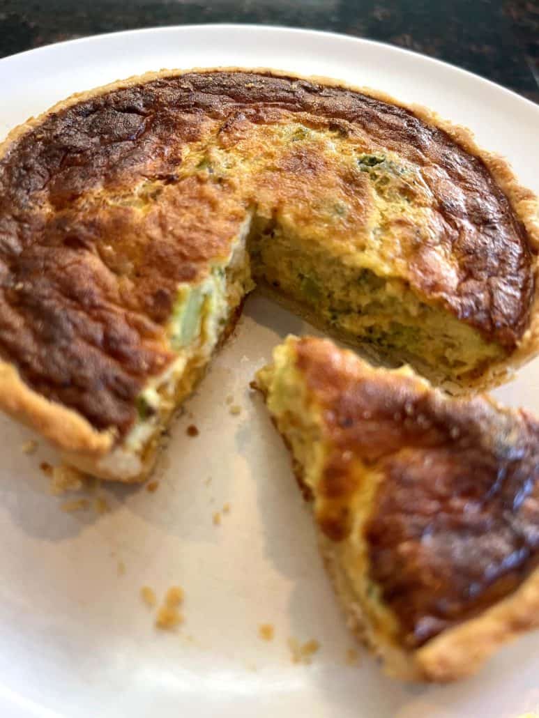 Zoomed-in view of a sliced broccoli and cheddar quiche on a plate, highlighting the creamy interior and crisp crust.