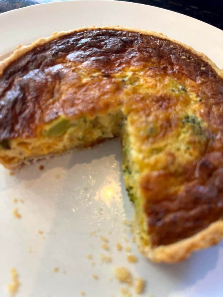 Partially sliced broccoli and cheddar quiche on a white plate, showing the golden crust and fluffy interior from the air fryer frozen quiche recipe.