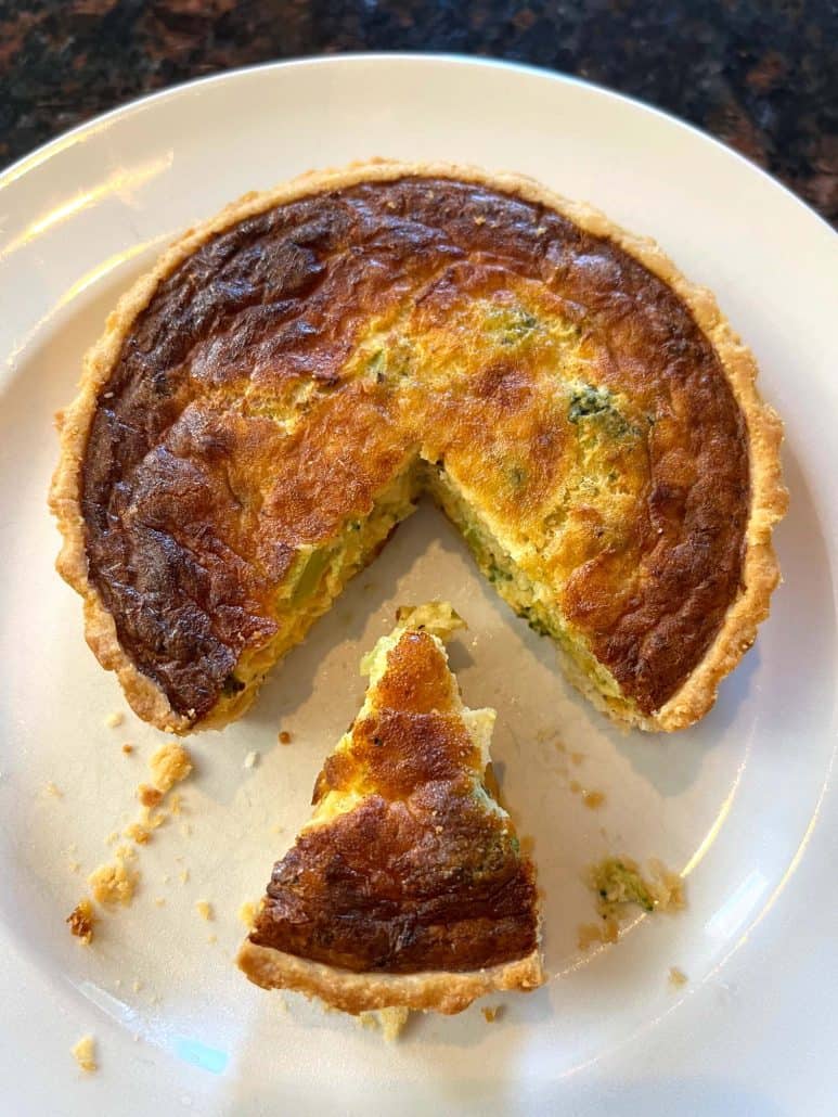 Cooked broccoli and cheddar quiche with a slice cut out, showing the flaky crust and creamy filling.