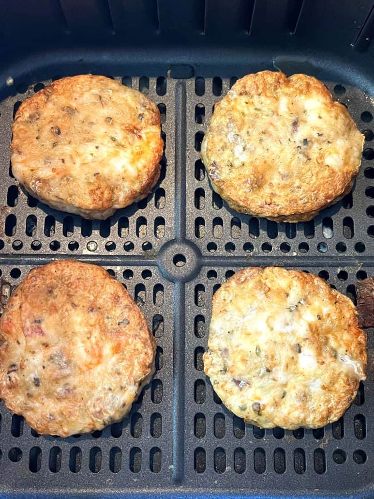 Close-up of four golden-brown shrimp burgers in an air fryer basket, perfectly cooked and ready to serve.
