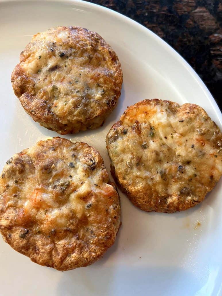 Close-up of three golden-brown shrimp burgers on a white plate, freshly cooked.