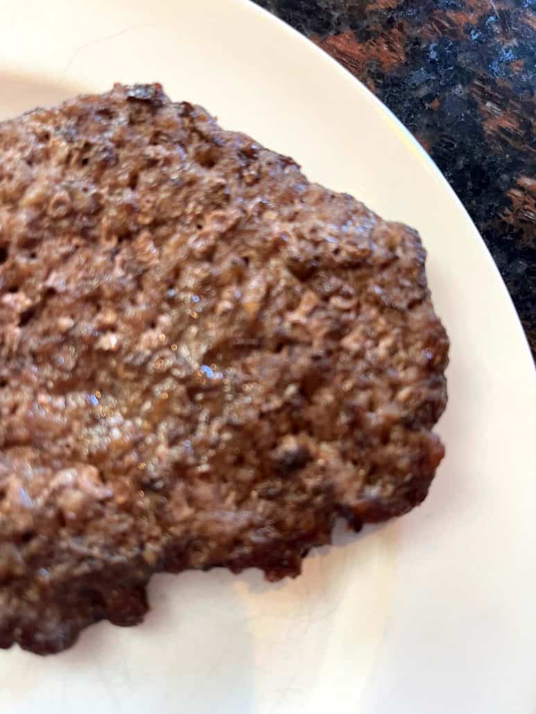 Cooked air fryer smashed burger patty served on a white plate, ready to be dressed with toppings or eaten as-is.