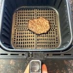 Cooked frozen smashed burger patty in air fryer basket after 9 minutes at 400°F, ready to be served.