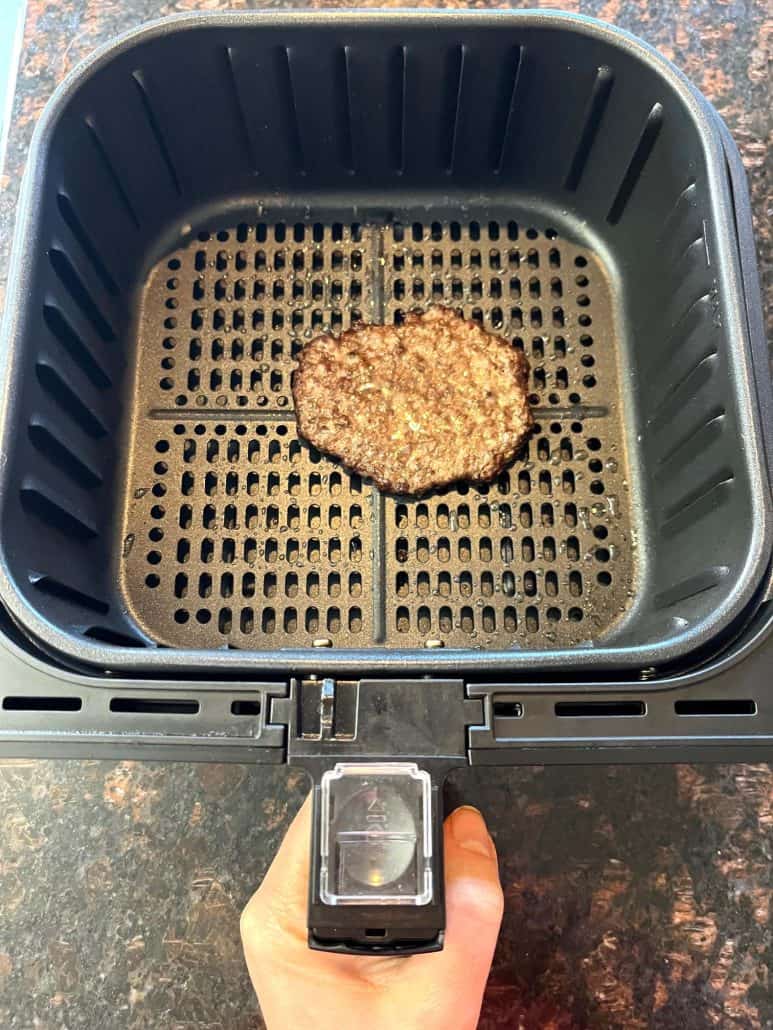 Cooked frozen smashed burger patty in air fryer basket after 9 minutes at 400°F, ready to be served.