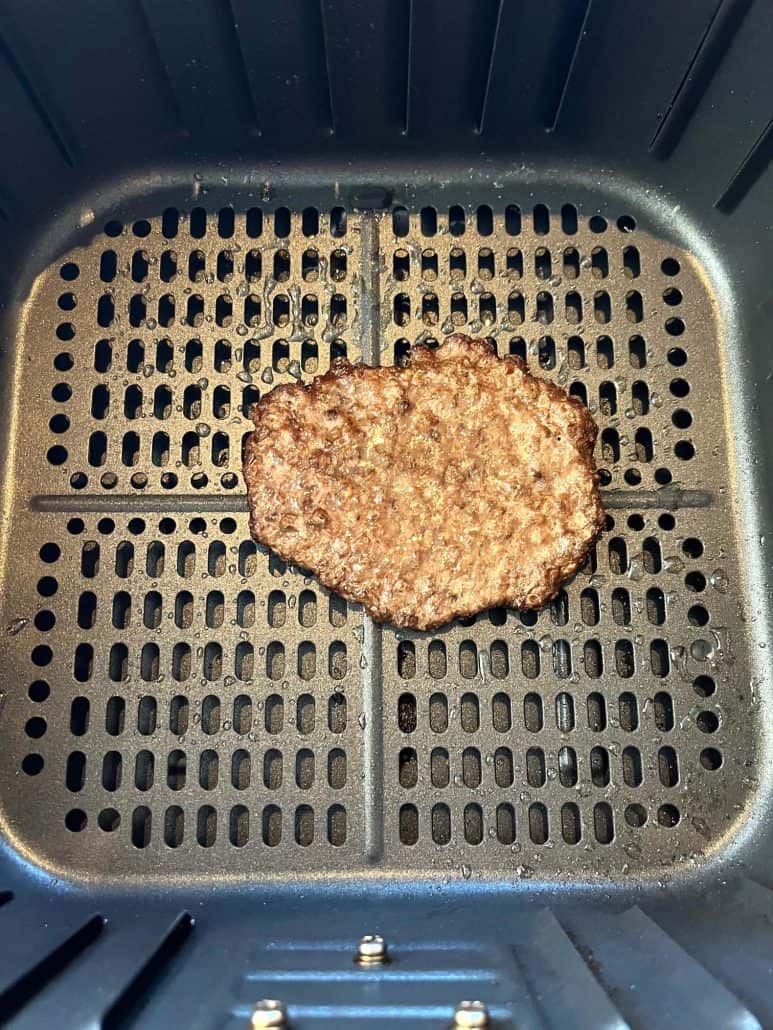Air fryer basket with a golden-brown smashed burger patty fully cooked and ready to be served.
