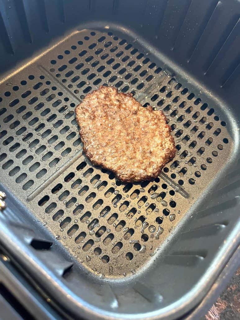 Fully cooked smashed burger patty in the air fryer basket, showing browned and crispy edges after air frying.