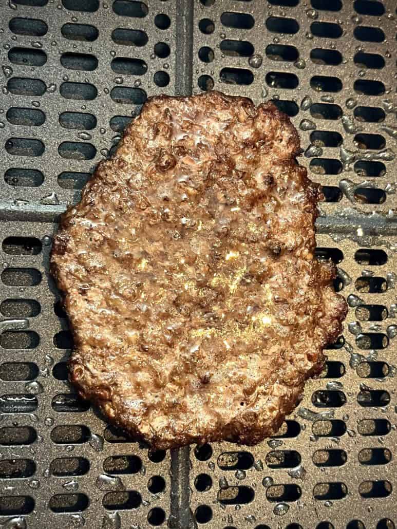 Close-up of a cooked smashed burger patty in the air fryer, showing browned texture and crisp edges after air frying from frozen.