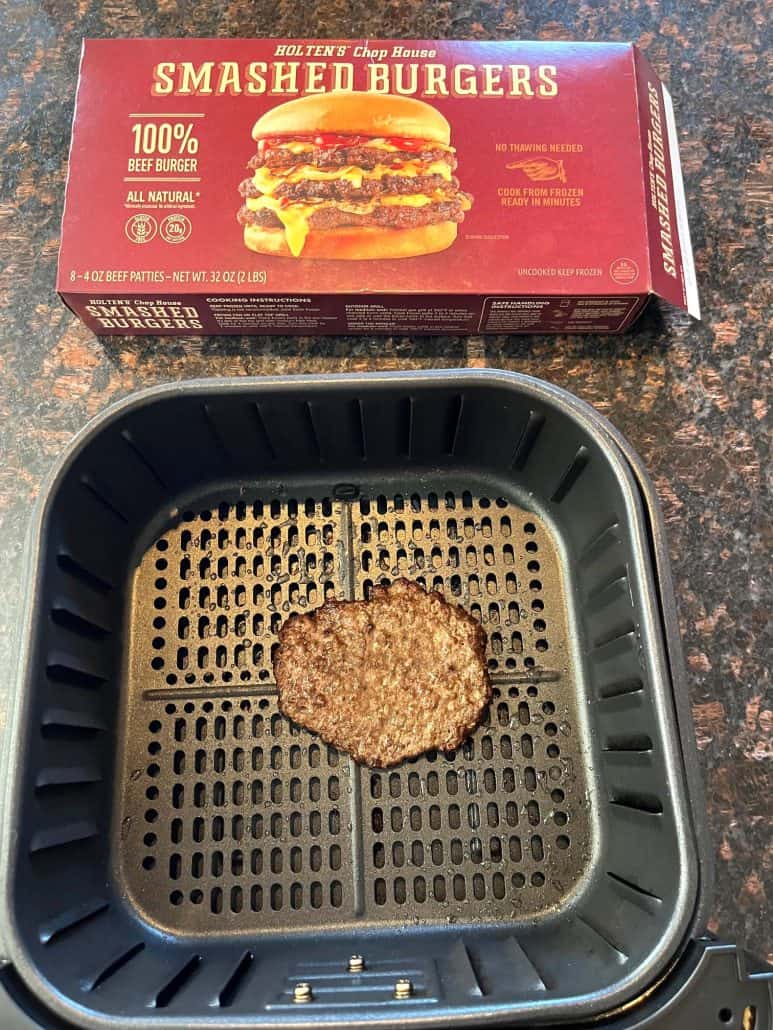 Cooked frozen smashed burger patty in air fryer basket with the burger box in the background, showing the final result straight from the air fryer.