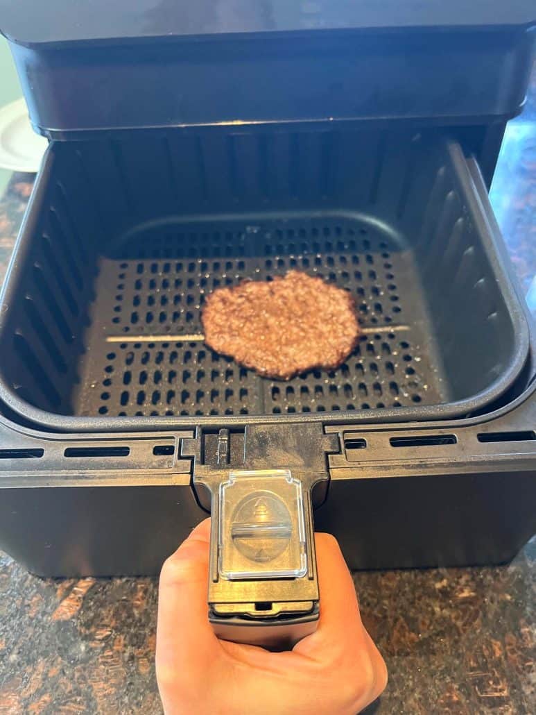 Placing a frozen smashed burger patty into the air fryer basket before cooking at 400°F for 9 minutes.