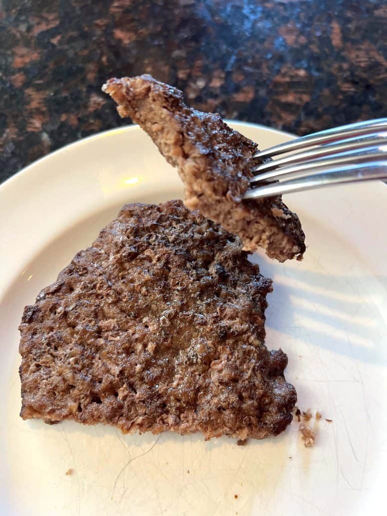 Air fryer smashed burger patty on a plate with a fork lifting a juicy bite to show the perfectly cooked inside.