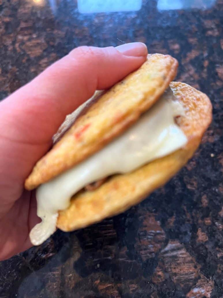 Hand of Melanie Mendelson from melaniecooks.com holding a freshly cooked, crispy texture and delicious Jimmy Dean Delights Egg’wich with melted cheese.