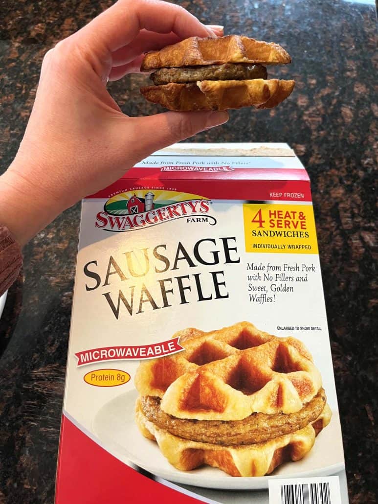 Melanie Mendelson of melaniecooks.com is holding a crispy Swaggerty's Farm Sausage Waffle Sandwich over the product box, showcasing the delicious air-fried result.