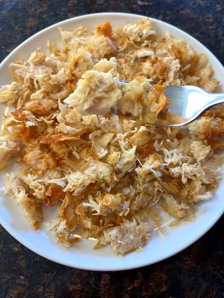 Fork lifting a bite of crispy air fryer shaved chicken breast from a plate.
