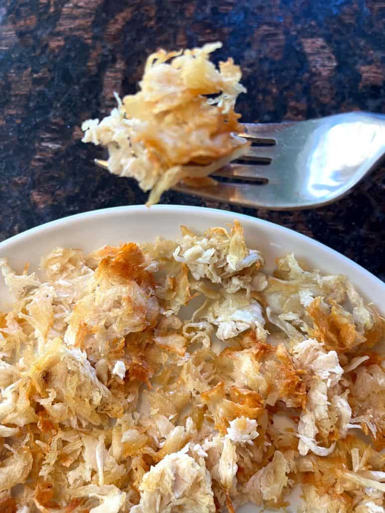 Fork holding a bite of crispy air fryer shaved chicken breast above a plate—highlighting the golden edges and tender texture of this easy, no-prep meal.