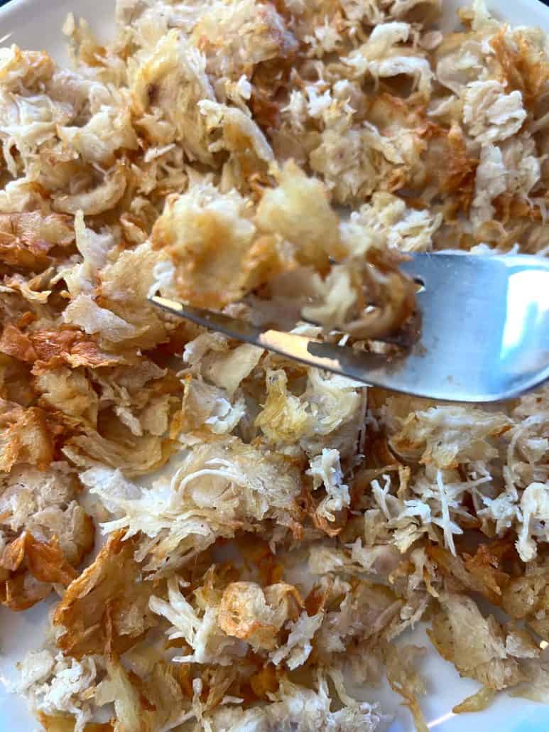 A fork scooping up crispy, golden bits of air fryer shaved chicken breast—showcasing the delicious texture.