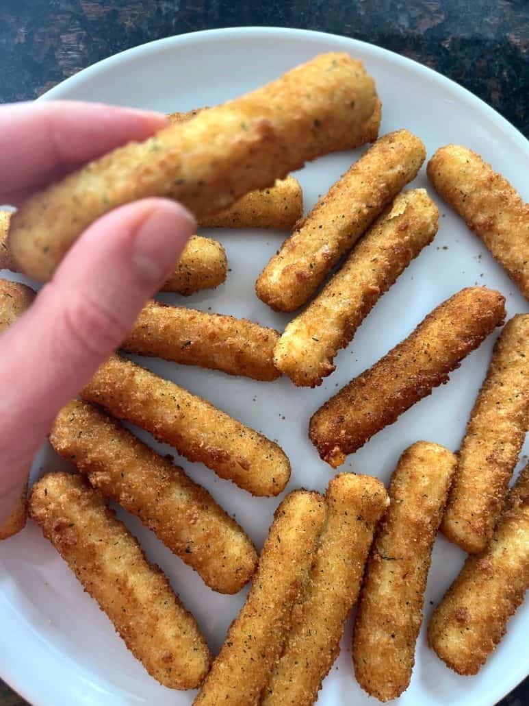 Melanie Mendelson from melaniecooks.com holding a crispy, golden mozzarella stick above a plate.