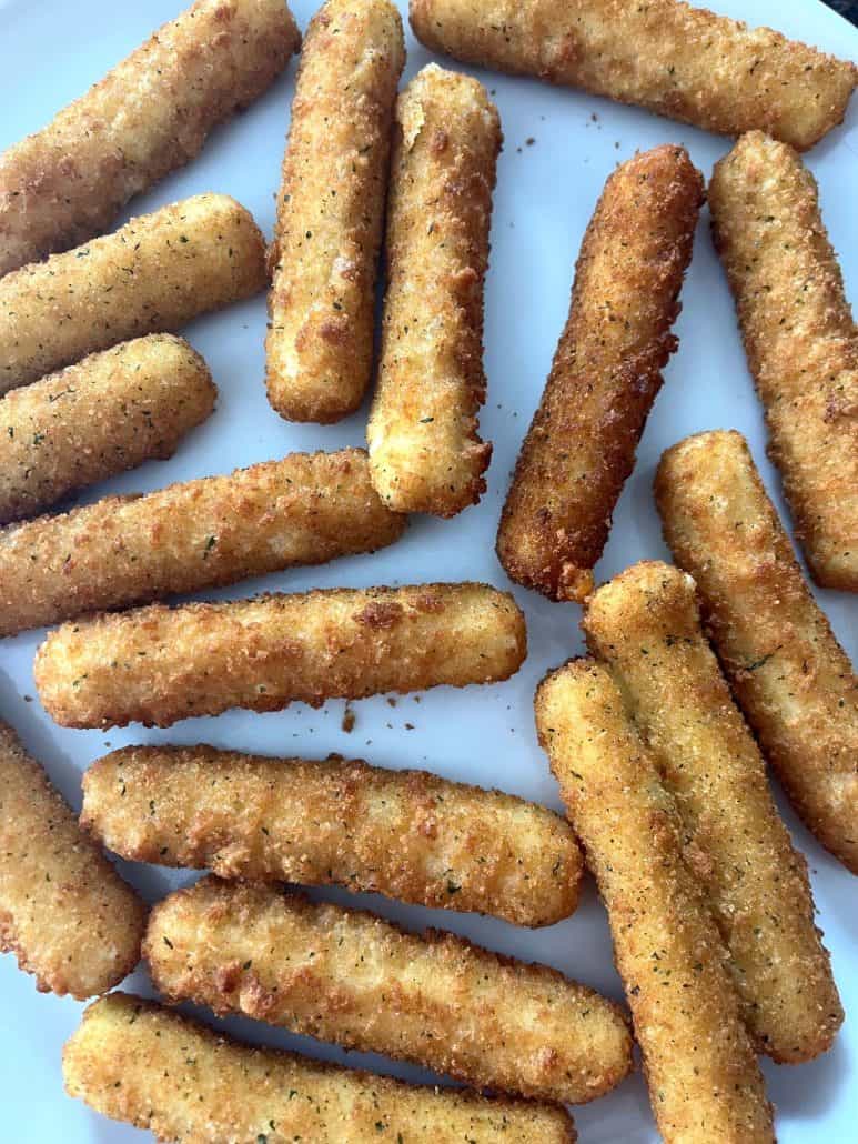 Close-up of crispy, golden air-fried mozzarella sticks arranged on a white plate.