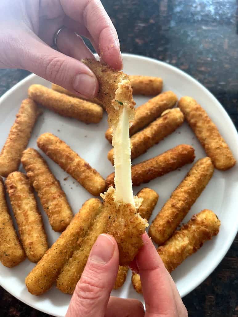 Melanie Mendelson from melaniecooks.com pulling apart a crispy mozzarella stick, revealing gooey, melted cheese.