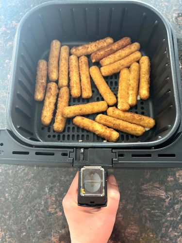 Air fryer basket filled with crispy, golden-brown mozzarella sticks, freshly cooked and ready to serve.