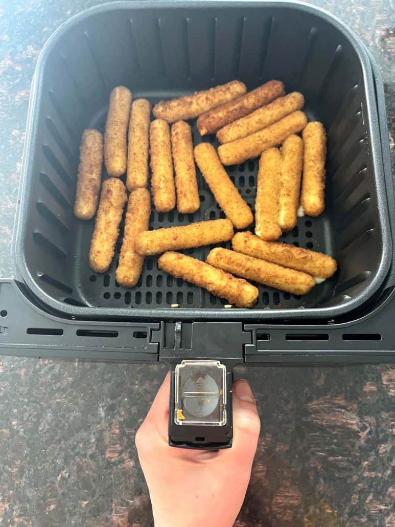 Air fryer basket filled with crispy, golden-brown mozzarella sticks, freshly cooked and ready to serve.