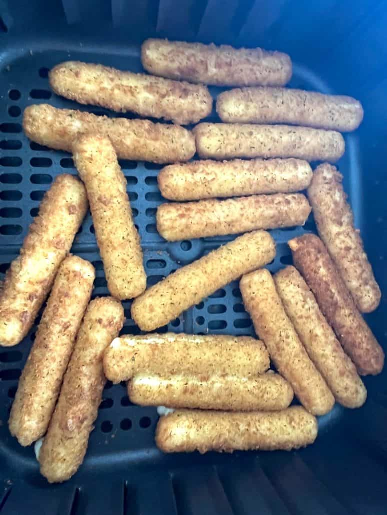 Close-up of golden, crispy mozzarella sticks evenly cooked in the air fryer basket.
