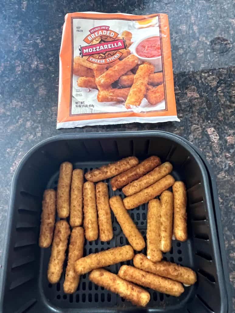 Air fryer basket filled with freshly cooked, crispy mozzarella sticks, with the Trader Joe’s packaging in the background.