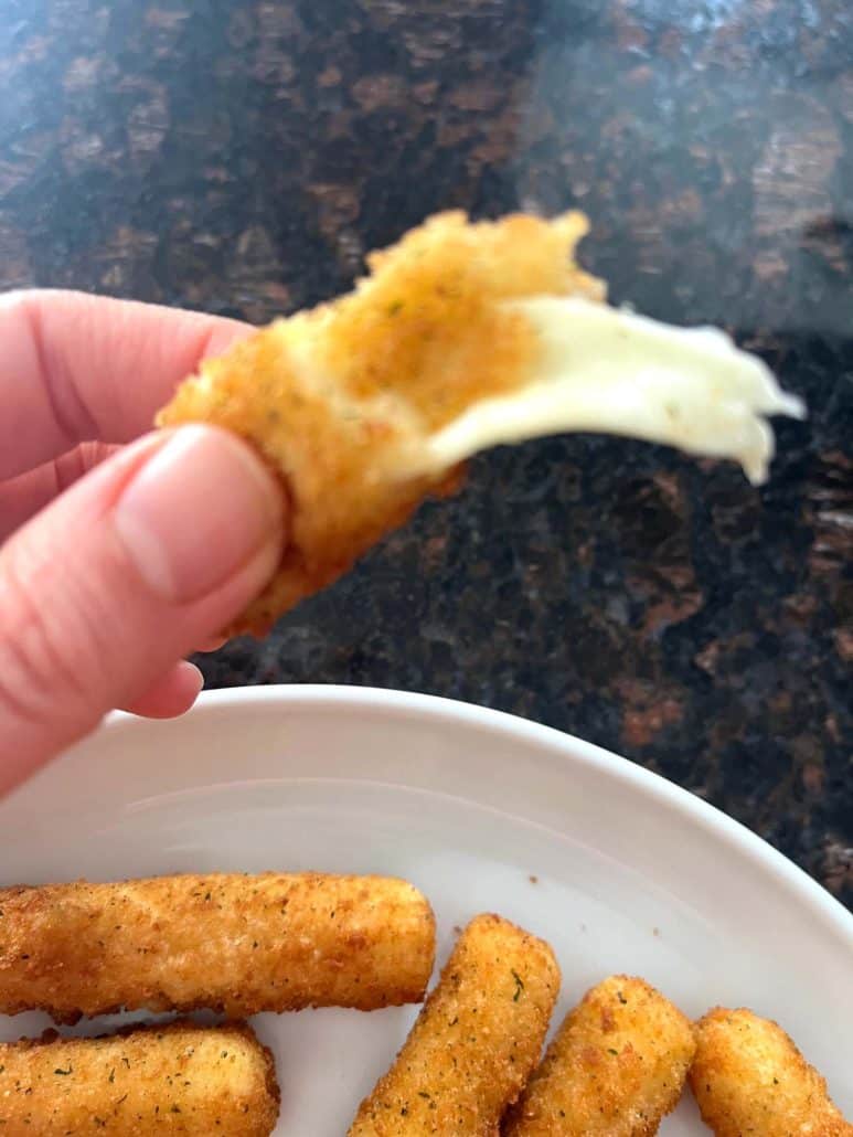 Melanie Mendelson from melaniecooks.com holding a crispy mozzarella stick with gooey, melted cheese stretching from the bite.