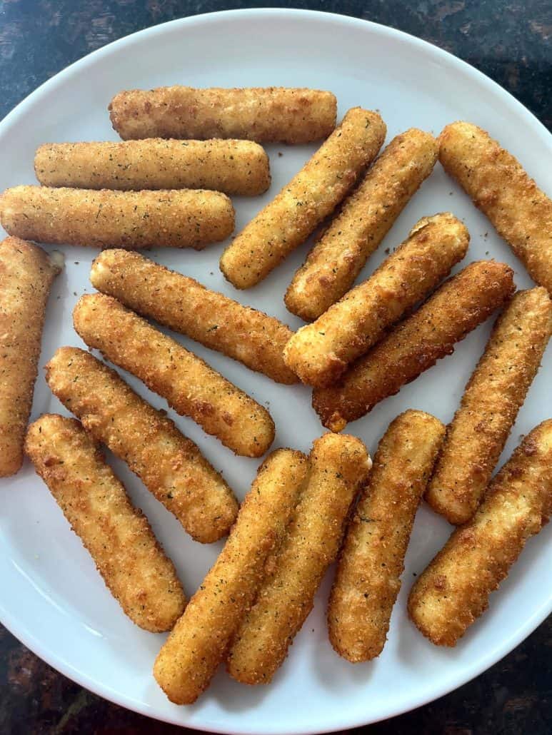 A plate full of crispy, golden-brown mozzarella sticks freshly cooked in the air fryer.