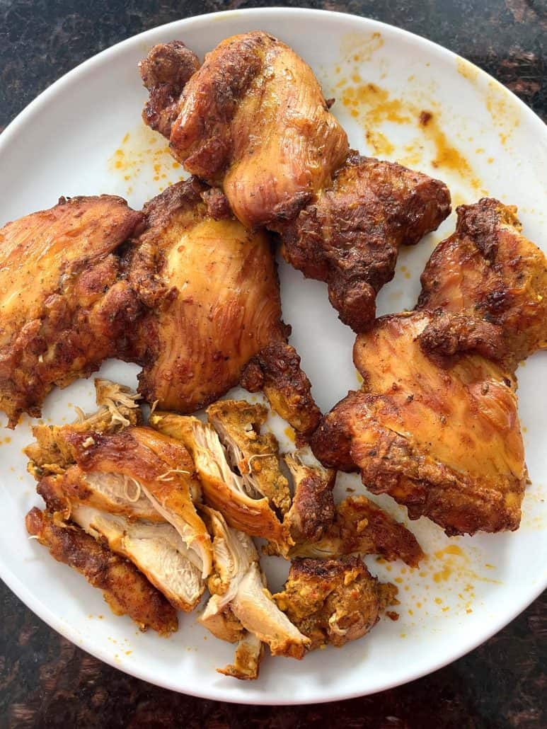 Cooked Trader Joe’s shawarma chicken thighs served on a white plate, with some pieces sliced and ready to eat.