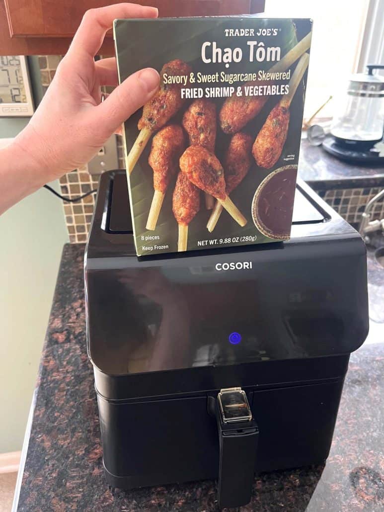 Melanie Mendelson from melaniecooks.com holding Trader Joe’s Chao Tom box above an air fryer, showing the product before cooking in this easy air fryer recipe.