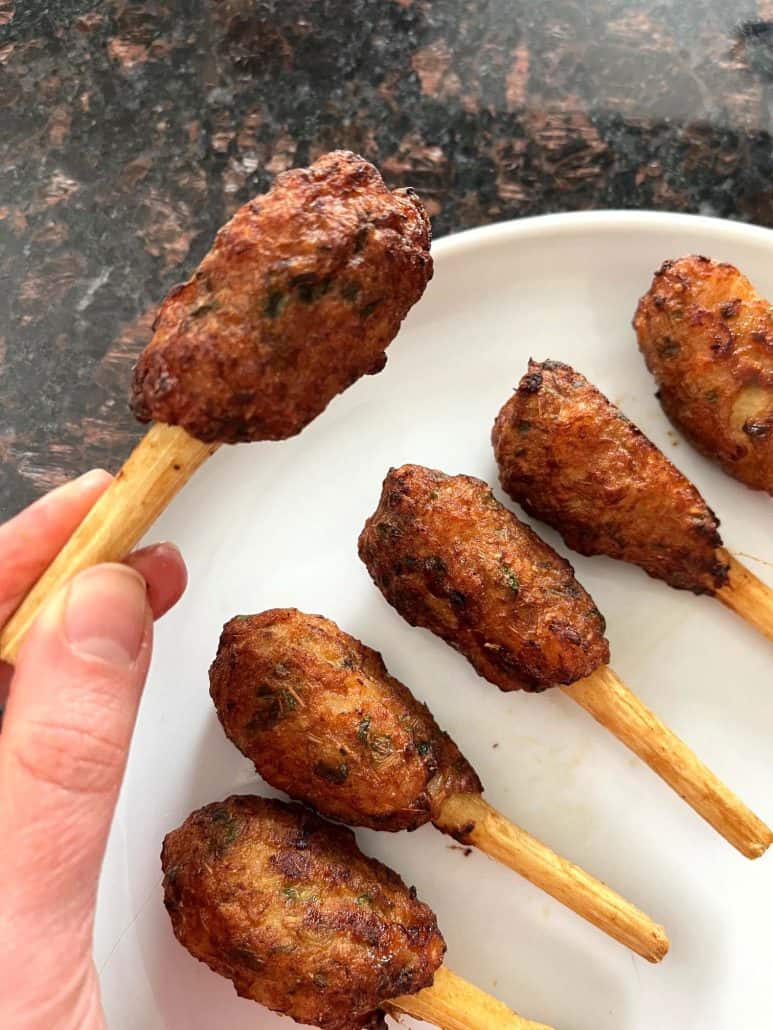 Melanie Mendelson from melaniecooks.com, holding a crispy cooked Chao Tom with more skewers on a plate.