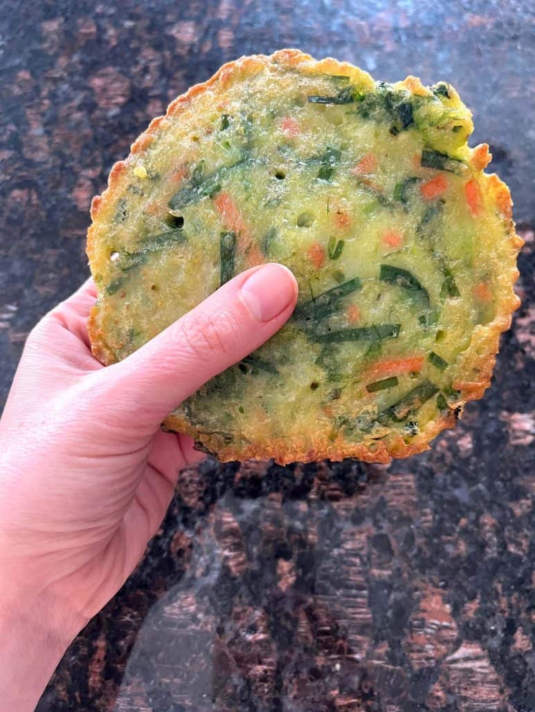 Hand of Melanie Mendelson from melaniecooks.com, holding a crispy Trader Joe’s scallion pancake, showing the perfectly cooked texture after air frying.