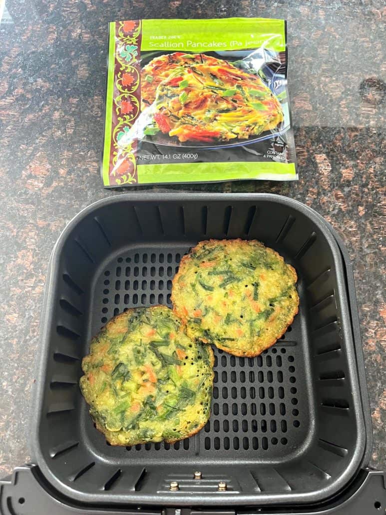Two cooked Trader Joe’s scallion pancakes in an air fryer basket with the empty pancake package in the background, showing the finished result using the air fryer cooking method.