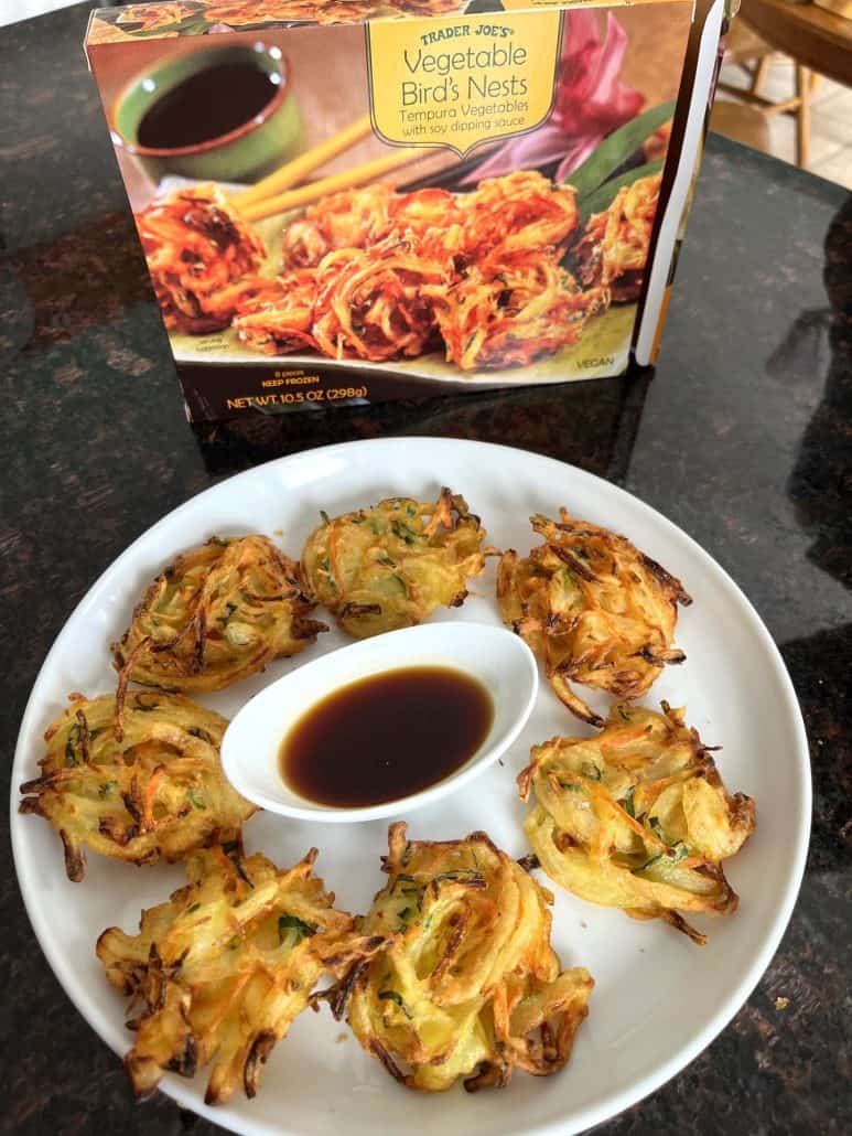 A plate of crispy, golden-brown Trader Joe’s Vegetable Bird’s Nests served with dipping sauce, with the original packaging in the background.
