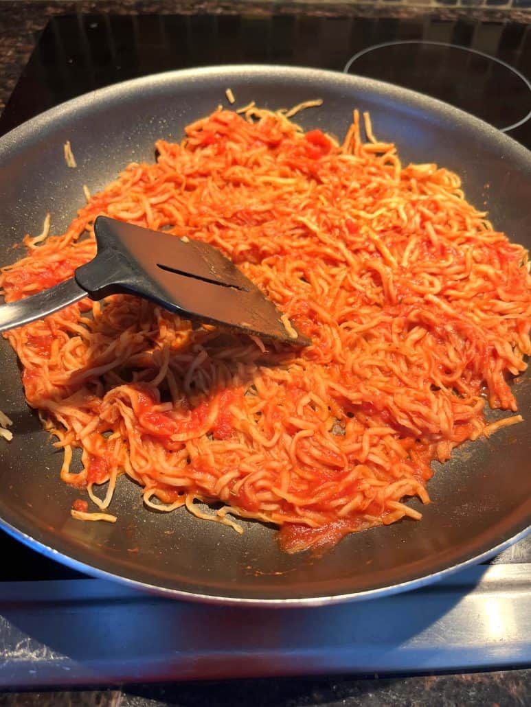 Hearts of palm pasta being stirred with a spatula in a frying pan, coated in marinara sauce.