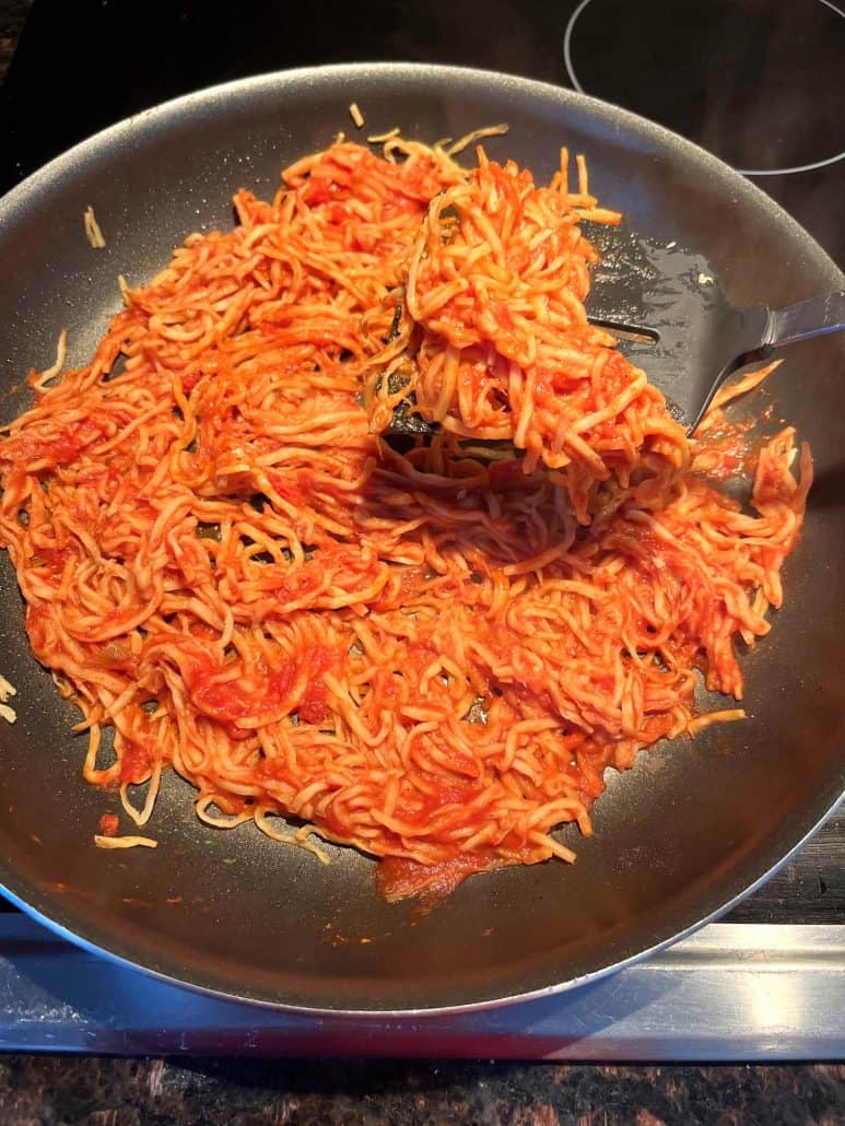 A spatula mixing hearts of palm pasta with marinara sauce in a frying pan, creating a delicious and healthy low-carb pasta alternative.